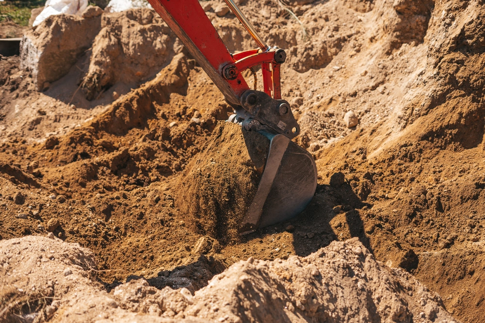 Łyżka koparki podnosząca ziemię na placu budowy – roboty ziemne