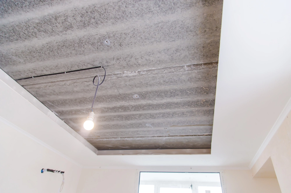 Sufit podwieszany w trakcie montażu, widoczne profile i surowa płyta stropowa z wiszącą żarówką