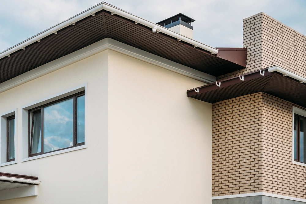 Okna zamontowane w elewacji domu z jasnym tynkiem i ceglaną ścianą pod dachem