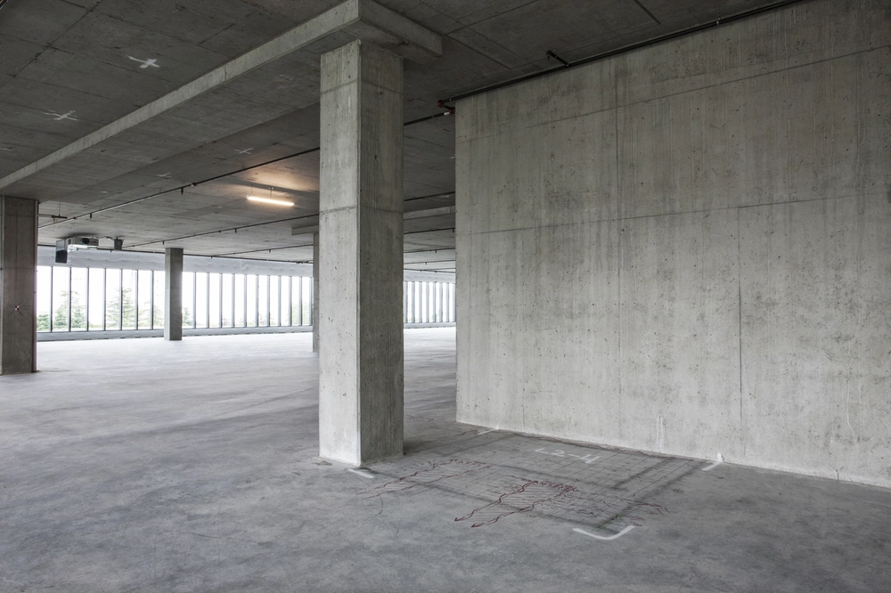 Widok wnętrza budynku z gładką, świeżo wykończoną posadzką przemysłową i betonowymi słupami